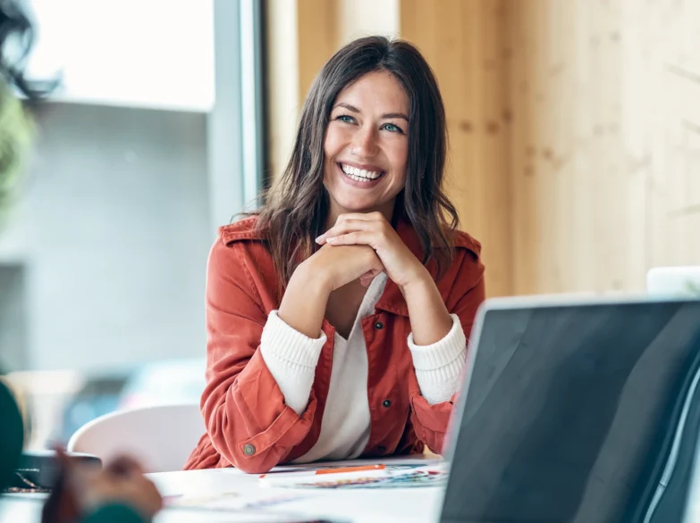 A woman smiling while sitting at a table, working on her laptop.
