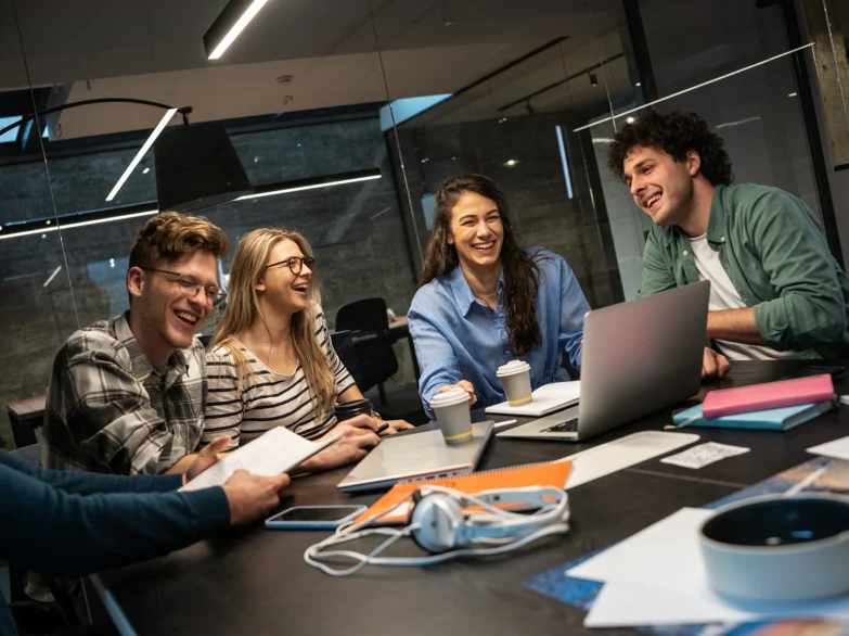 A group of young people collaborating around a table, each using their laptops for a project or discussion.
