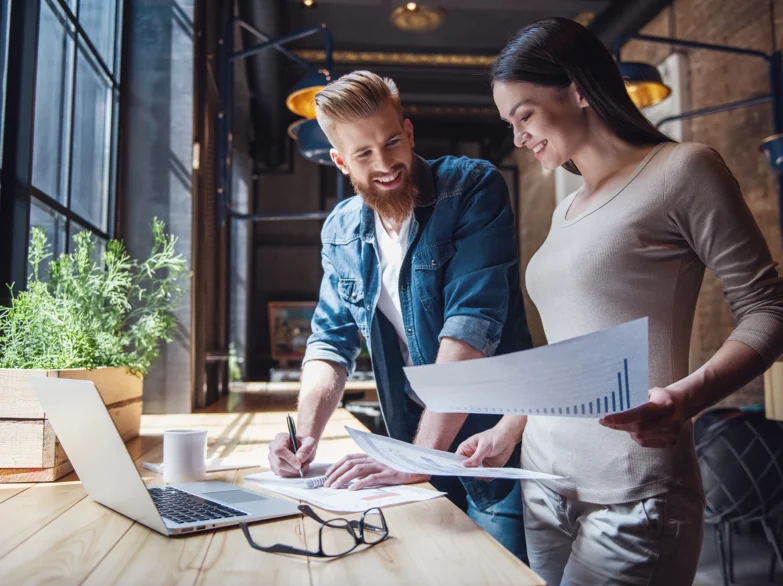 A man and woman are reviewing documents together on a laptop, focused and engaged in their discussion.