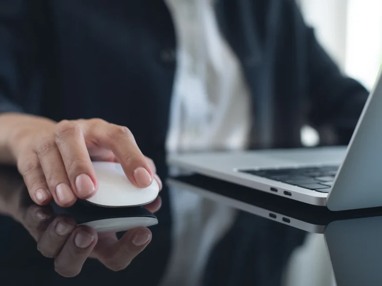 A person using a mouse while working on a laptop computer at a desk.